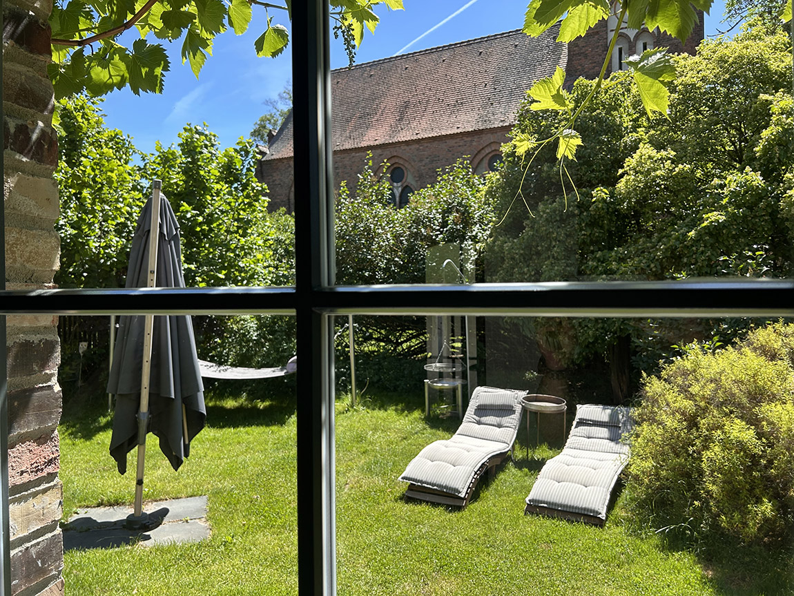 Durch die im Weinlaub eingerahmten Sprossenfenster fällt der Blick auf den privaten Garten und die historische Kirche nebenan. | HYGGE HAUS: Entschleunigung hat eine Adresse